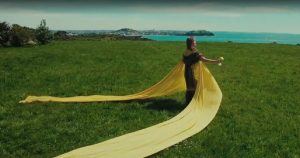 Precious Clark standing on Takaparawhau holding poi with sunshine banners streaming from her across the grass