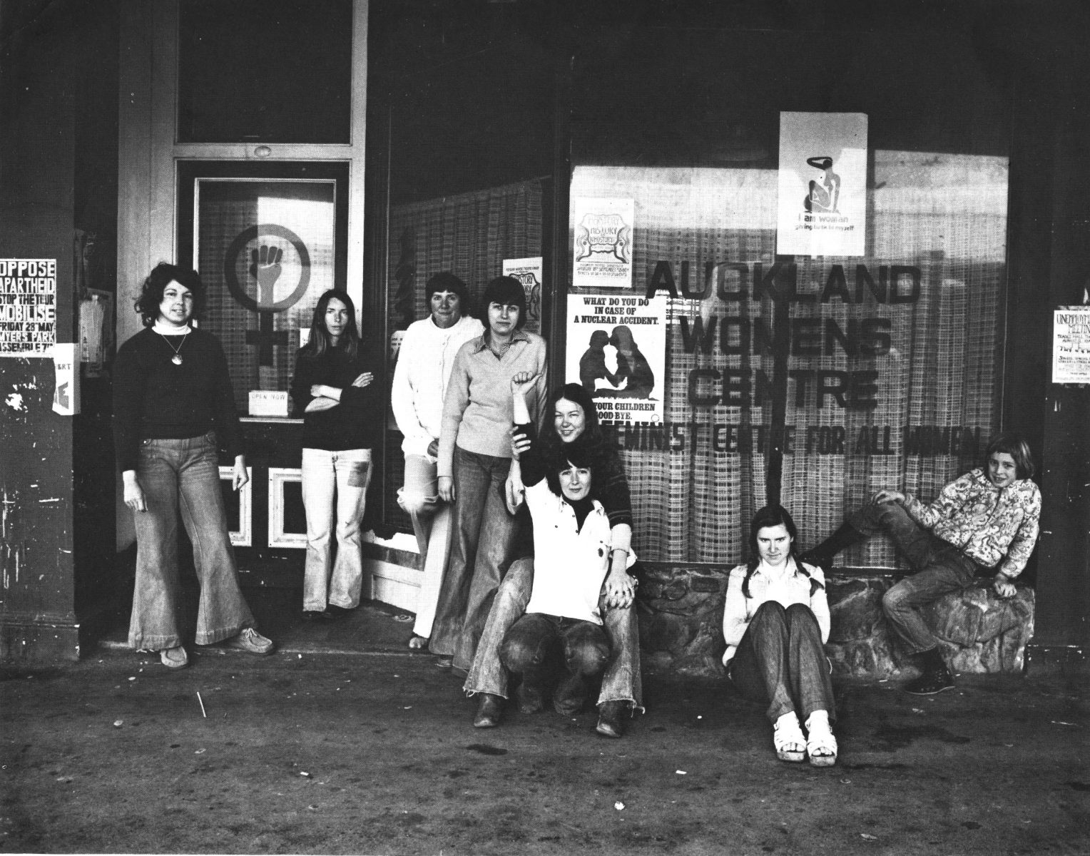 women in 1975 in front of a window with "Auckland Women's Centre" stencilled on it