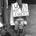 someone wearing a bird costume with a sign: "women are not chicks" black and white image